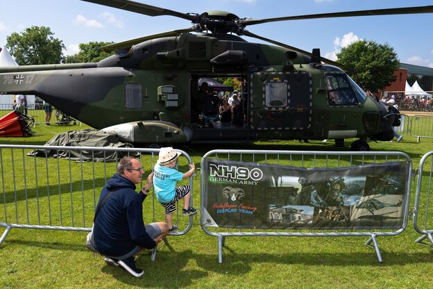 An Mann und ein Kind stehen an einer Absperrung vor einem Militärhubschrauber