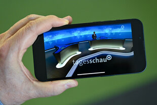 Eine Person hält ein Smartphone, auf dem der Tagesschau-Sprecher Constantin Schreiber zu sehen ist