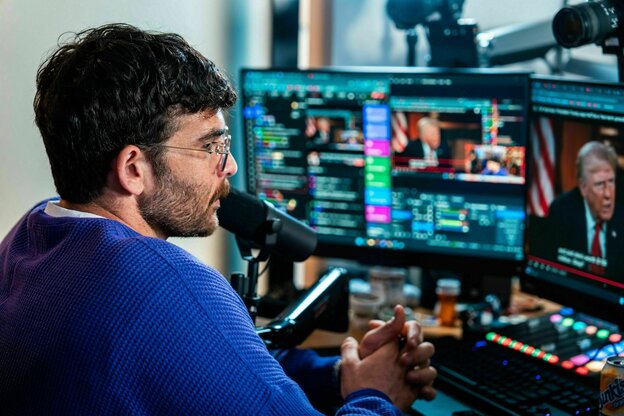 Der Streamer sitzt im blauen Pulli vor vielen Bildschirmen und spricht ins Mikro