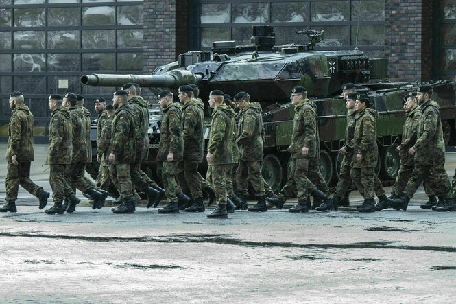 Bundeswehrsoldaten marschieren an einem Kampfpanzer Leopard 2A6 vorbei