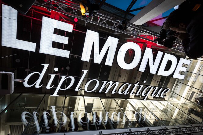 Die legendäre alte Leuchtreklame von Le Monde diplomatique hängt heute von der Decke des Speisesaals der tat Kantine im taz-Neubau – Symbol kritischer Öffentlichkeit, fotografiert bei einer Abendveranstaltung.