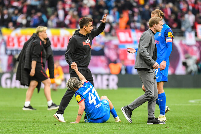 Trainer hilft Spieler hoch und klatscht einen anderen ab