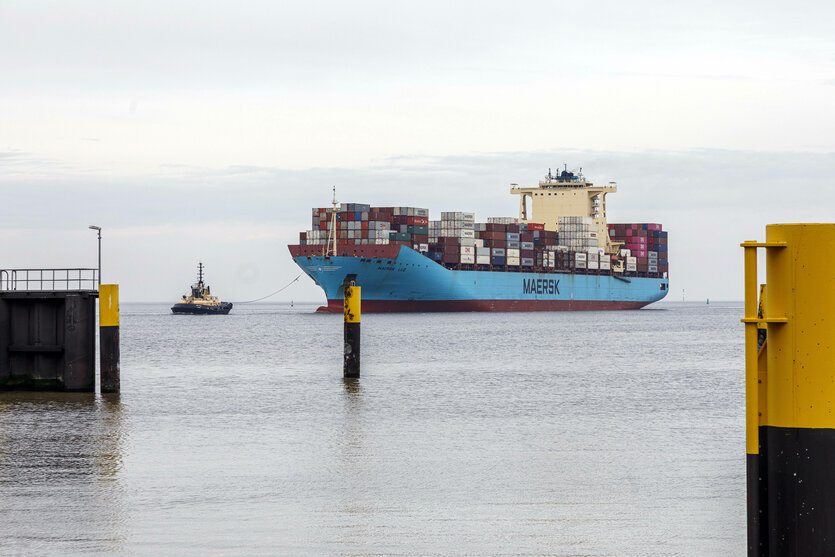 Ein Schlepper geleitet ein Containerschiff in einen Hafen