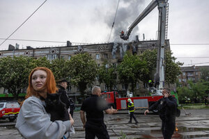 Eine Frau hält eine Katze im Arm, im Hintergrund steht ein Kran der Feuerwehr vor einem brennenden Gebäude