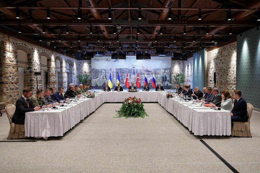 Personen sitzen an einem U-förmigen Tisch, im Hintergrund Fahnen der Ukraine und Russlands, in der Mitte die der Türkei
