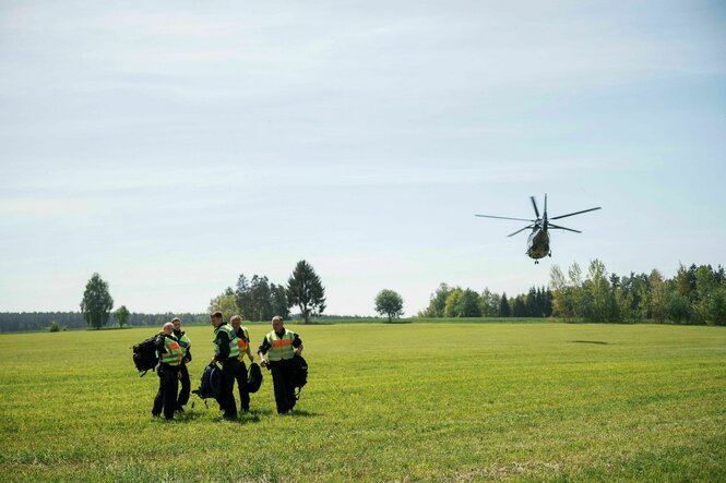 Bundespolizisten stehen auf einem Feld, im Hintergrund dreht ein Hubschrauber ab