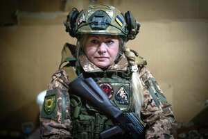 Eine Frau mit blondem Zopf in Uniform. Sie hält ein Maschinengewehr in den Händen