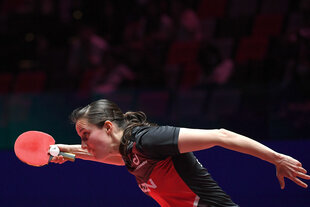 Eine Sportlerin hält einen Tischtennisschläger in der Hand und schaut konzentriert auf den Ball