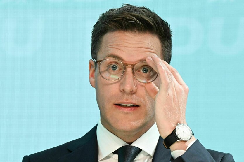 Manuel Hagel hebt eine Hand an seine runde Brille