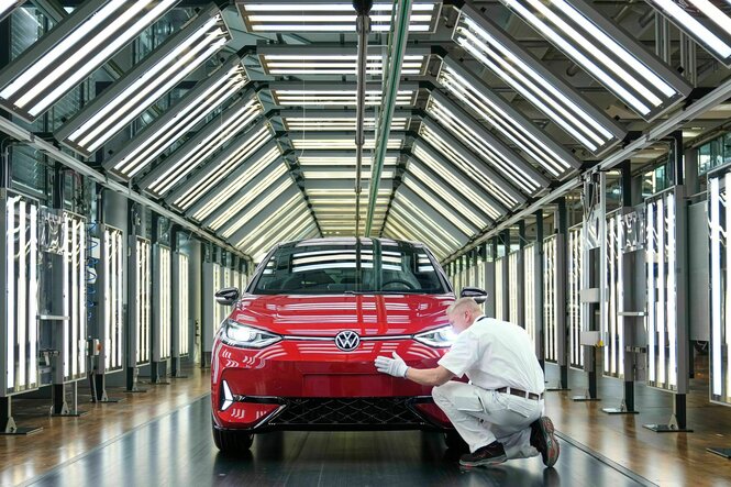Eine Person streicht mit weißen Handschuhen über die Front eines roten VW-Fahrzeuges in einer lichtdurchfluteten Halle
