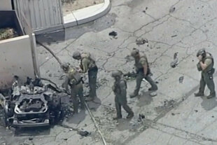 Schwer uniformierte Polizisten begutachten ein Autowrack