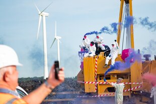 Zu sehen sind Aktivist:innen der Gruppe „Ende Gelände” auf einem Baustellengefährt mit farbigen Rauchbomben und Overalls.