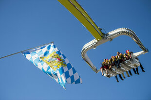 Ein Fahrgeschäft auf dem Oktoberfest vor einer Bayernflagge