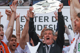 Ein Mann hält die Meisterschale in die Höhe, um ihn herum junge Sportler, die ihm zujubeln.