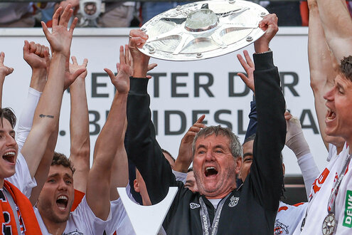 Ein Mann hält die Meisterschale in die Höhe, um ihn herum junge Sportler, die ihm zujubeln.
