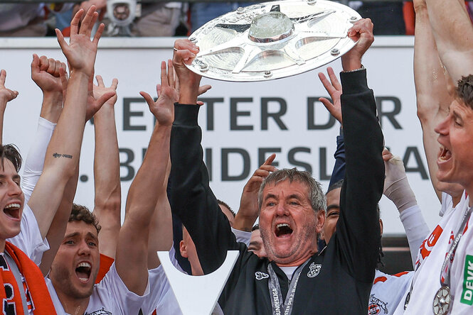 Ein Mann hält die Meisterschale in die Höhe, um ihn herum junge Sportler, die ihm zujubeln.