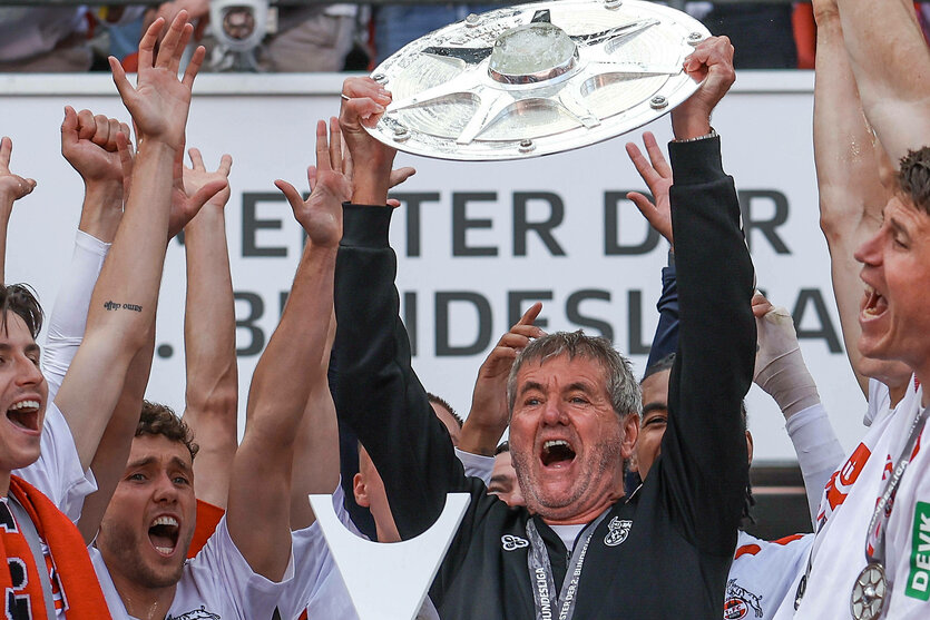 Ein Mann hält die Meisterschale in die Höhe, um ihn herum junge Sportler, die ihm zujubeln.