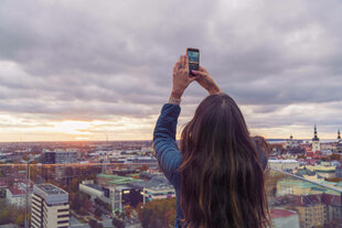 Rückenansicht einer Person, die ihr Smartphone in die Höhe streckt, vor ihr die Skyline von Tallinn