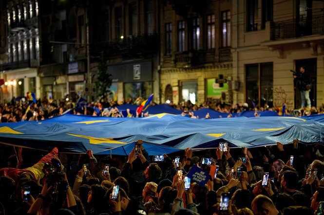 Eine Menschenmenge mit erhobenen Handys und einer riesigen EU Flagge, die über ihren Köpfen schwebt