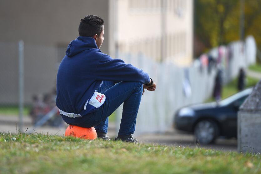 Jugendlicher sitzt auf einem Ball vor einer Container-Unterkunft für Geflüchtete