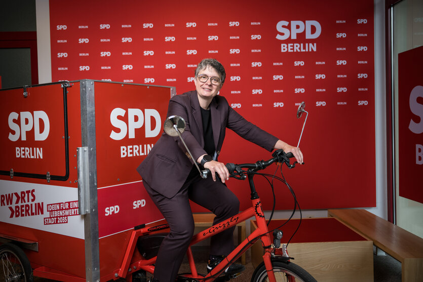 Eine Frau sitzt auf einem roten Fahrrad vor einer roten Wand