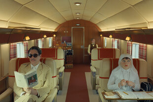 Filmszene aus „The Phoenician Scheme“, eine Gruppe Menschen sitzt im Flugzeug, sieht schick aus und ist zeitlich irgendwo in den 1950ern
