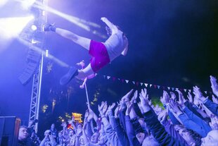 EIne Person fällt von einer Bühne in eine Menschenmenge zum Crowdsurfen