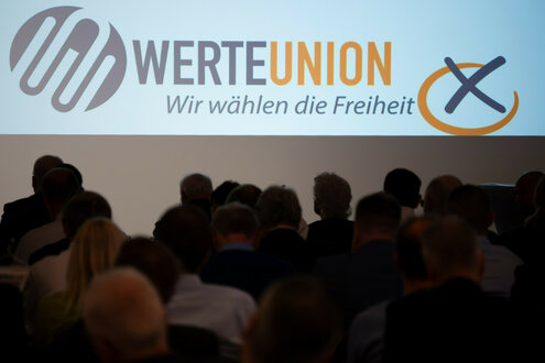 Männer mit grauen Haaren versammeln sich zum Bundepsarteitag der Werteunion. Sie drehen der Kamera den Rücken zu