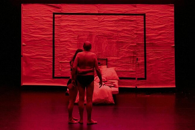 Ein rot glimmender Hintergrund auf einer ansonsten dunklen Theaterbühne