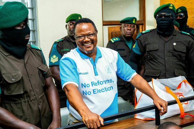Tundu Lissu lacht, er ist von Uniformierten umringt