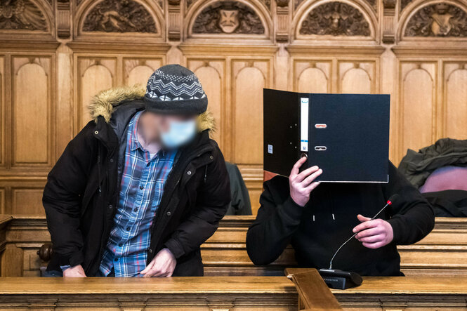Angeklagten Dave S. und Nico J. vor dem Bremer Landgericht mit medizinischer Maske und Ordner vor dem Gesicht.