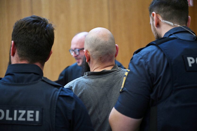 Zwei Polizisten führen ein Mann mit Glatze in einen Gerichtssaal