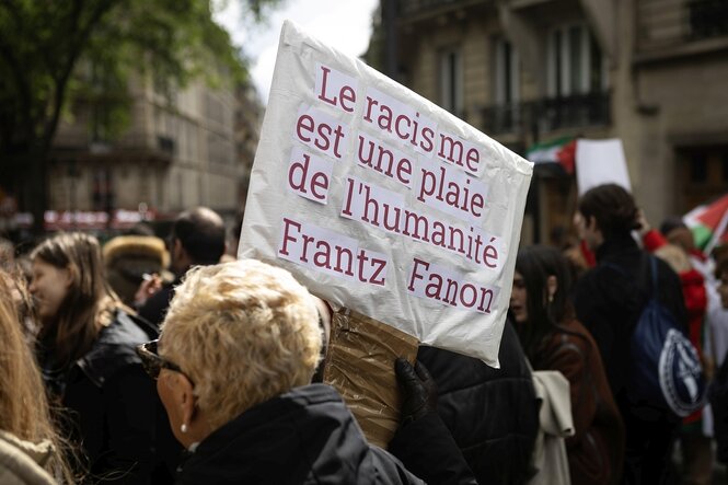 Eine Frau trägt ein Plakat mit einem Zitat von Frantz Fanon