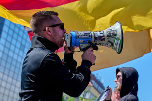 Eine junger Neonazi hält ein Mikrofon vor einer Deutschlandfahne