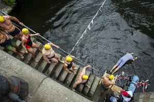 In Badekleidung steigen die Schwimmer:innen die Treppe zur Spree hinunter. Einer von ihnen macht einen Köpfer.