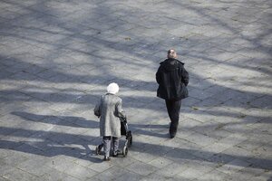 Eine alte Frau geht mit einem jüngeren Mann spazieren. Sie hat einen Rolator
