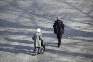 Eine alte Frau geht mit einem jüngeren Mann spazieren. Sie hat einen Rolator