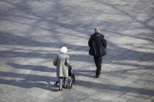 Eine alte Frau geht mit einem jüngeren Mann spazieren. Sie hat einen Rolator