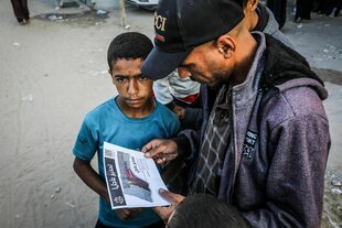 Ein Mann liest ein Flugblatt in arabischer SChrift, ein Junge steht daneben
