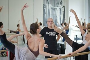 Ein Mann steht zwischen übenden Balletttänzerinnen, er trägt ein T-Shirt mit der Aufschrift Stuttgarter Ballet: Ex-Ballettintendant Reid Anderson zieht offenbar weiterhin die Strippen in Stuttgart.