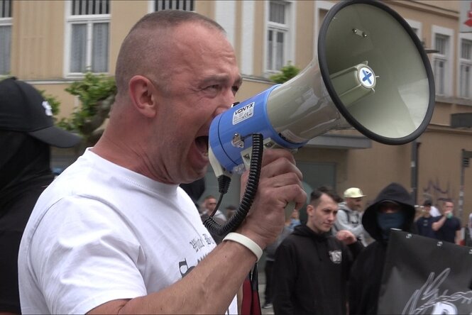 Ein Mann mit Glatze und in weißem T-shirt schreit in ein Megafon