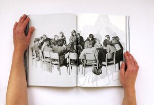Hände halten ein aufgeschlagenes Buch, das eine Schwarz-Weiß-Fotografie von Menschen zeigt