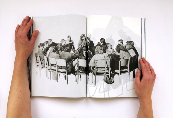 Hände halten ein aufgeschlagenes Buch, das eine Schwarz-Weiß-Fotografie von Menschen zeigt