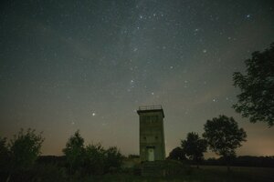 Der alte Grenzturm steht umgeben von Bäumen in der Landschaft, über ihm wölbt sich der Sternenhimmel