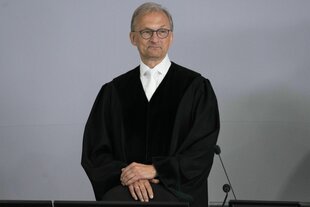 Porträt des Richters Jürgen Bonk in schwarzer Robe, er steht an seinem Richtertisch und lächelt milde