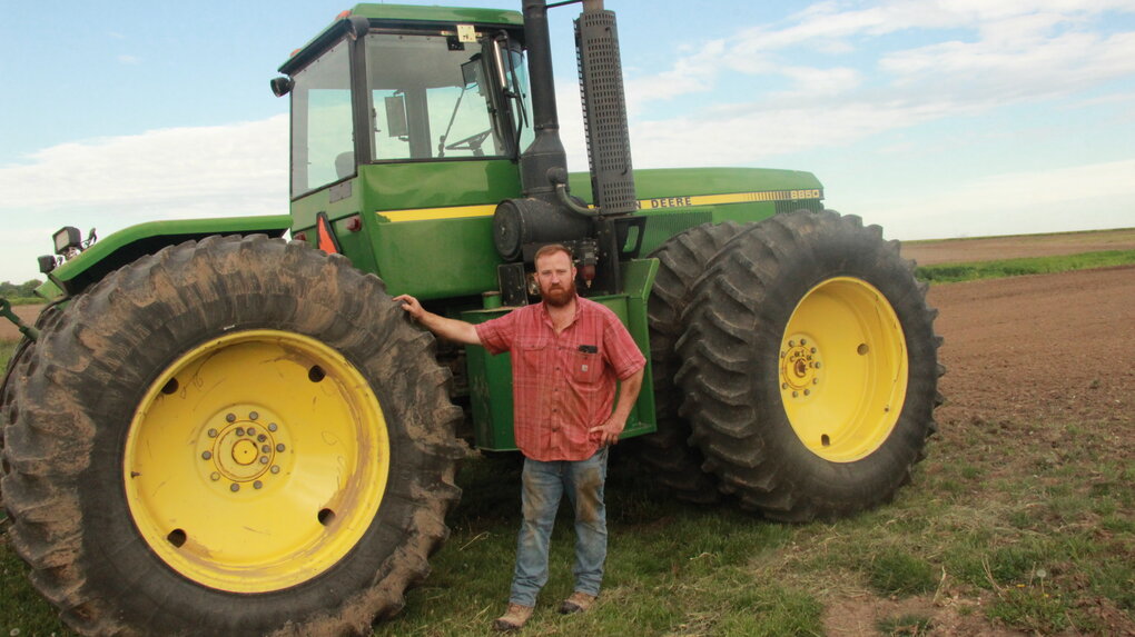 Ein Bauer steht an seinem Traktor auf dem Feld
