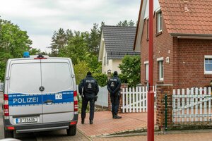 Polizeiwagen und Polizistne stehen vor einem rot geklinkerten Reihenhaus