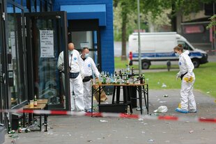 Zwei Polizisten und eine Polizsitin in weißer Schutzkleidung an einem Tatort