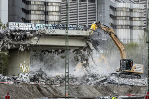 Ein Bagger reißt die Berliner Westendbrücke ab. Es staubt. Im Hintergrund stehen Wohngebäude.