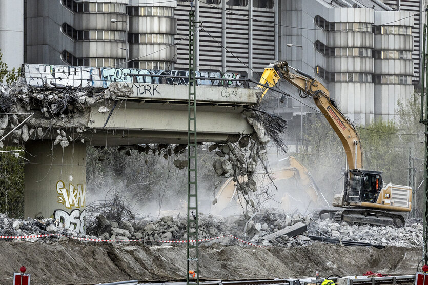 Ein Bagger reißt die Berliner Westendbrücke ab. Es staubt. Im Hintergrund stehen Wohngebäude.